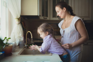 a mother helps her preschooler daughter wash her hands in their home kitchen
