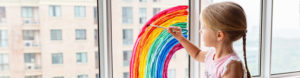 A child paints a rainbow on a window