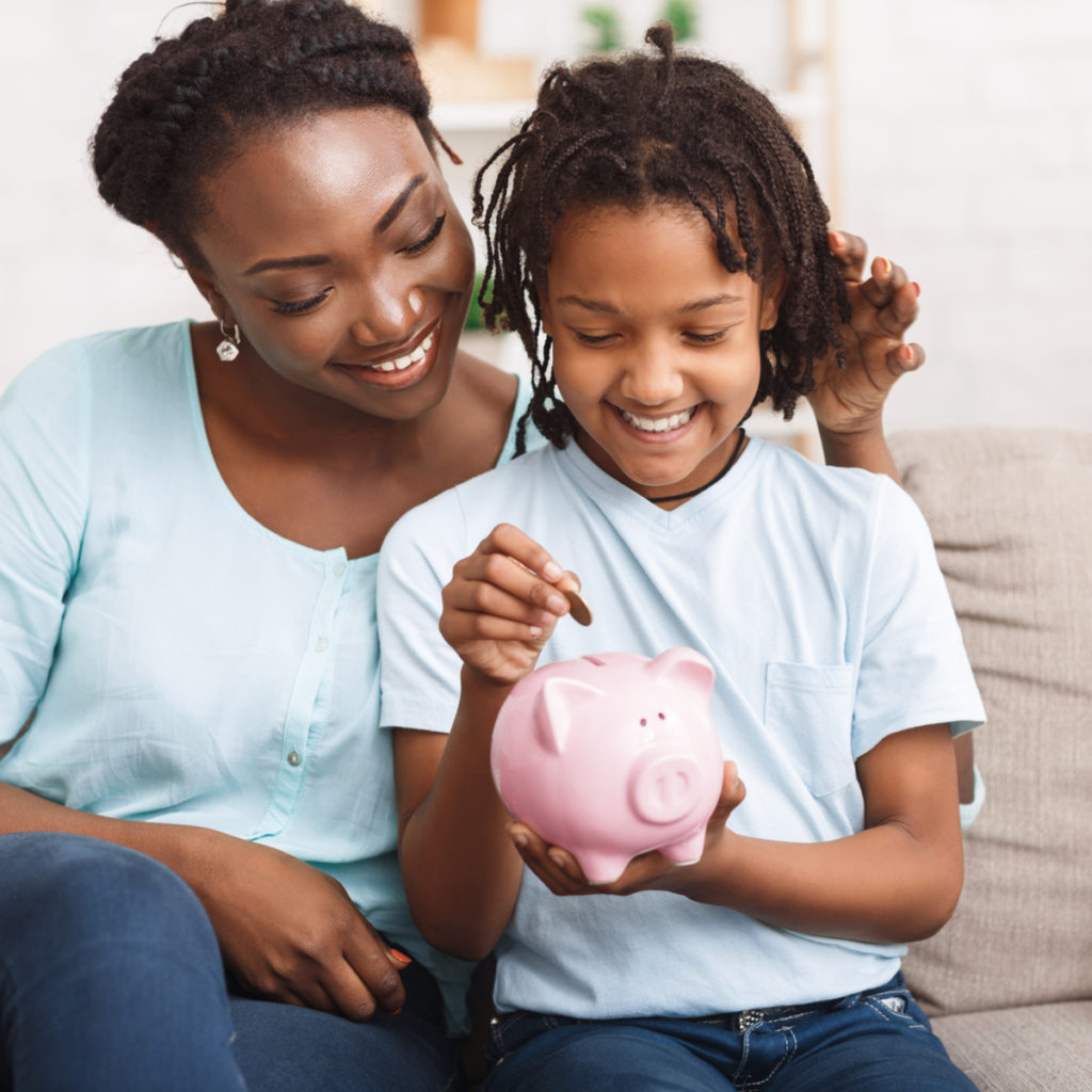 A mother helps her daughter add money to a piggy bank